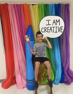 a young boy sitting on a chair with a sign in front of him that says i am creative