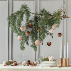 the table is set for christmas dinner with pine branches and ornaments hanging from the ceiling