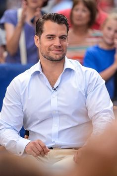 a man sitting in front of a crowd with his hands on his hips and looking at the camera