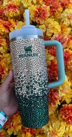 a hand holding a blue and green coffee cup in front of flowers