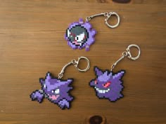 three pixel keychains are shown on a wooden surface, one is purple and the other is black