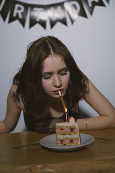 a young woman blowing out a candle on a piece of cake that is sitting on a plate