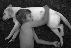 a young boy laying on the ground next to a white dog with it's head under his arm