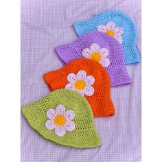 three crocheted hats with flowers on them sitting on a purple cloth covered bed