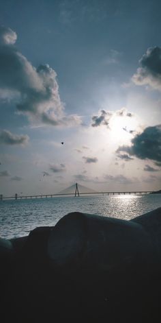 the sun shines brightly through clouds over the ocean and bridge in the distance,