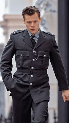 a man in uniform walking down the street with his hand on his hip and looking at something