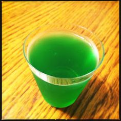 a glass filled with green liquid sitting on top of a wooden table