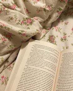 an open book sitting on top of a bed next to a white comforter covered in pink flowers