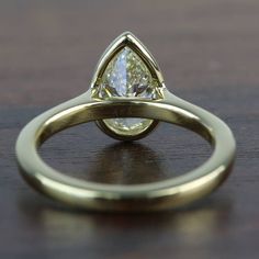 a yellow gold ring with a pear shaped diamond in the center on a wooden surface