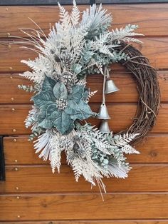 a wreath with silver bells and greenery is hanging on a wooden wall next to a door