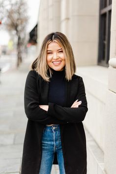 a woman standing in front of a building with her arms crossed and looking at the camera