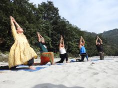 five people are doing yoga on the sand in front of some trees and mountains,