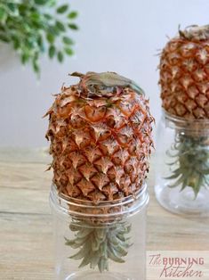 two pineapples sitting in glass jars on a table