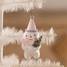 a snowman ornament hanging from a christmas tree with white ornaments and feathers