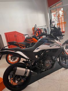 two motorcycles are parked in a showroom with orange accents on the tires and rims