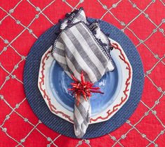 a blue plate topped with a silver and red napkin on top of a red table cloth