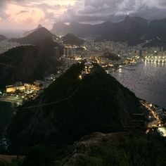 an aerial view of the city lights and water at night from atop a hill with mountains in the background