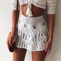 a woman wearing a white crochet skirt and crop top with tassels