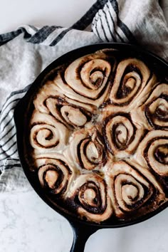 a pan filled with cinnamon rolls on top of a white table cloth next to a fork