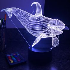 a 3d dolphin lamp sitting on top of a table next to a remote control and pen