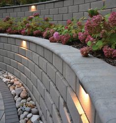 a stone wall with flowers growing on it and some lights in the corner next to it