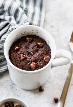 a white mug filled with chocolate cake on top of a table next to a spoon