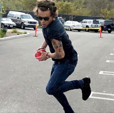 a man with tattoos is skateboarding in the parking lot while holding a red ball