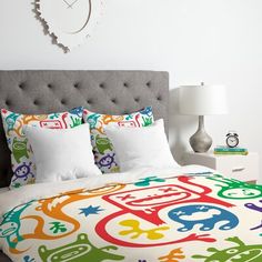 a bed with colorful comforter and pillows on it in a bedroom area next to a clock