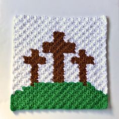 a cross stitched on top of a piece of cloth with grass and trees in the background