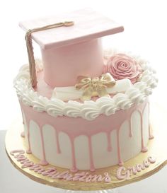 a cake decorated with pink icing and white frosting has a graduation cap on top