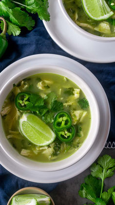 two white bowls filled with soup and garnished with cilantro, limes, and sliced jalapenos