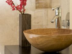 a wooden bowl sitting on top of a counter next to a vase with flowers in it