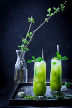 two glasses filled with green drinks on top of a tray