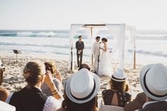 a couple getting married on the beach with their wedding party watching them walk down the aisle