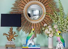 two parrots sitting on a table in front of a mirror and vase with flowers