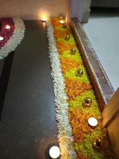 candles are lit on the ground in front of flowers and grass that have been cut into strips