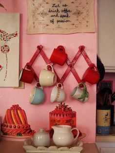 tea cups and cakes are hanging on the wall in front of a pink painted kitchen