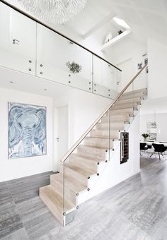 a staircase with glass railing and wooden handrails in a white room, leading up to the dining area