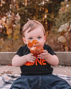 a little boy sitting on top of a blanket eating something with his hands and looking at the camera