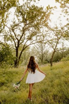 a woman in a white dress is walking through the grass