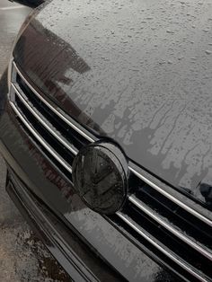 the front end of a black car with rain drops on it