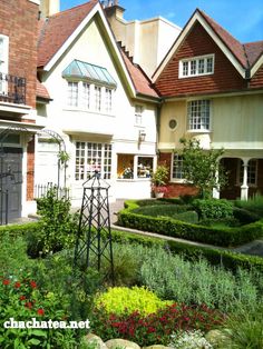 a house with lots of plants and flowers in the front yard, along with other houses