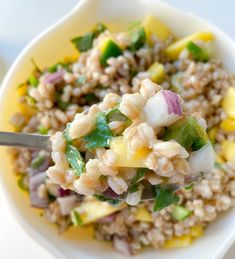 a bowl filled with rice and vegetables on top of a white table next to a fork