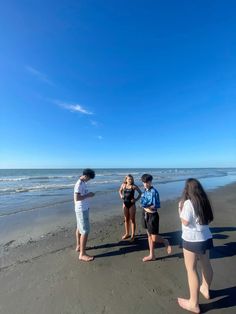 four people are standing on the beach and one person is taking a photo with her cell phone