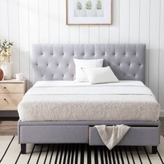 a bed with a gray headboard and foot board in a white room next to a black and white striped rug