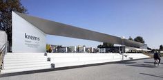 people are walking down the street in front of a large white building with a curved roof