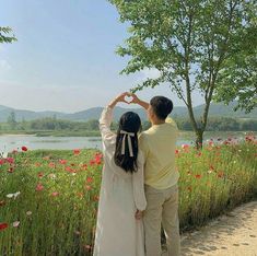 a man and woman standing next to each other in front of a field with flowers