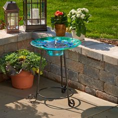 a blue bird bath sitting on top of a metal stand next to potted plants