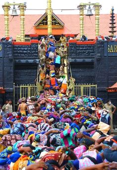 a large group of people standing in front of a building with statues on the roof