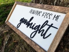 a wooden sign that says always kiss me goodnight on the side of a tree trunk